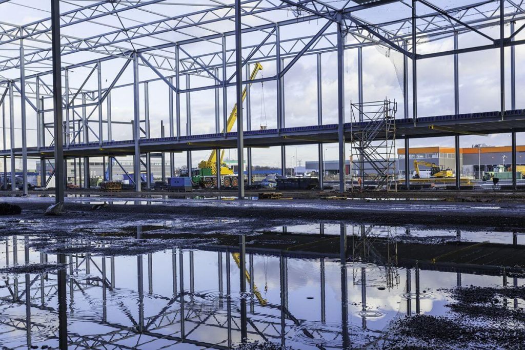 Steel building framework at a construction site with standing water after heavy rainfall