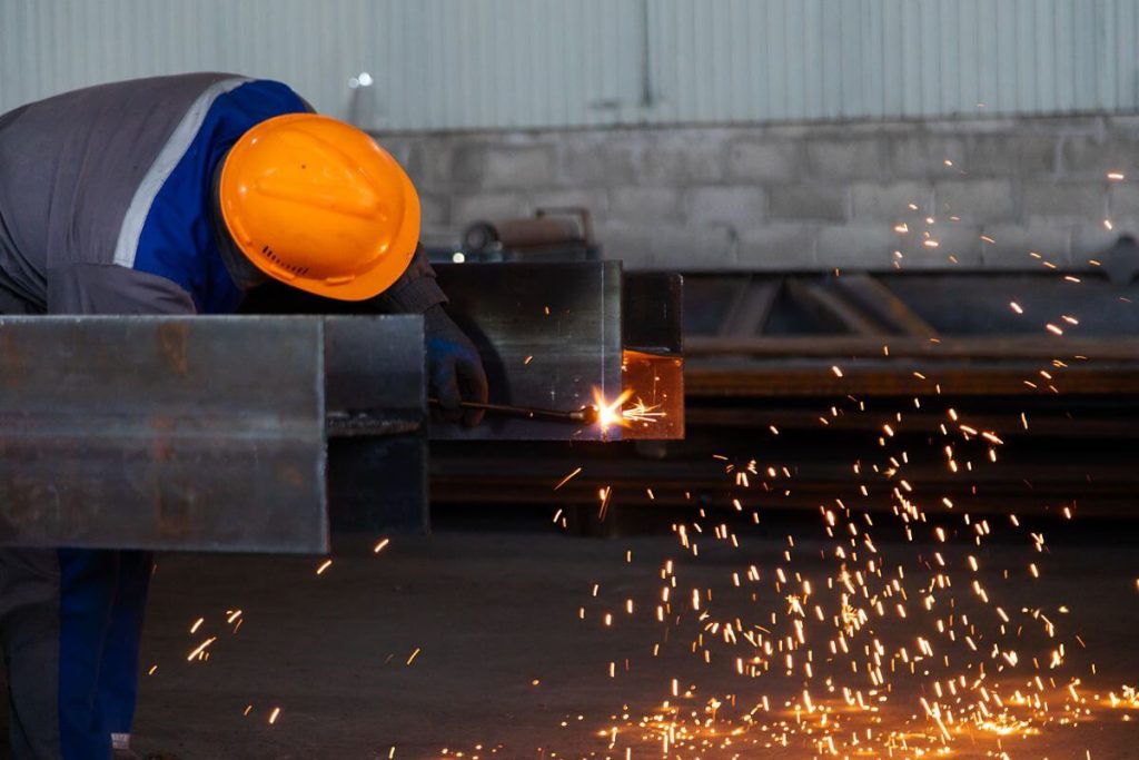 Steelworker welding structural steel components as sparks scatter inside an industrial facility